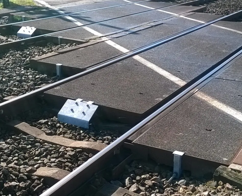 Level crossing with concrete crossing plates and a galvanised NIOP tensioner beside the rail