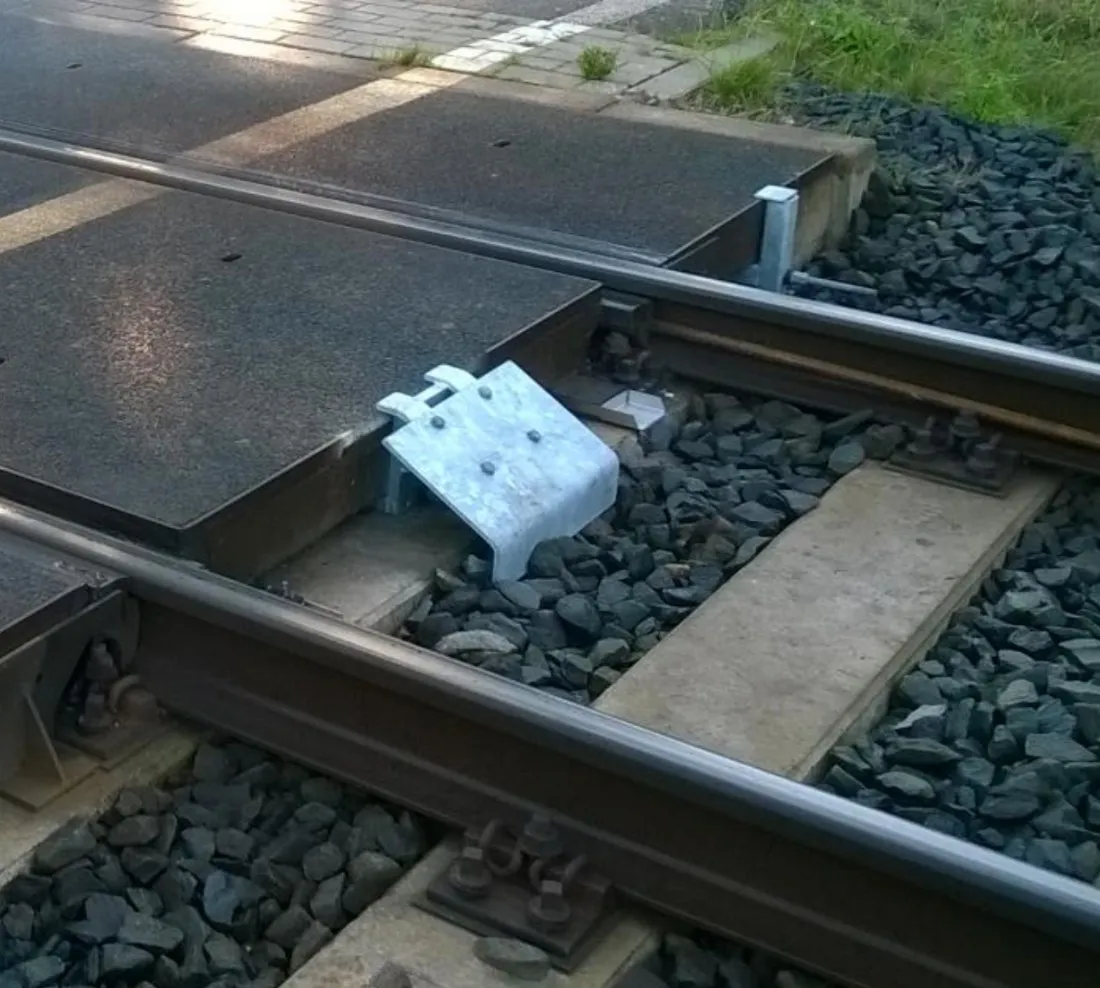 Galvanised NIOP tensioner at a UNI level crossing, between the concrete plates and the rail.